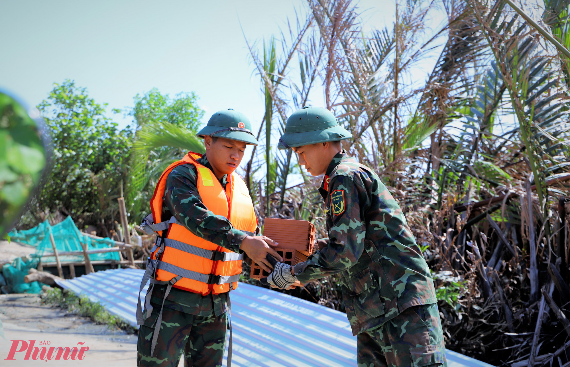  Các chiến sĩ bộ đội chuyền tay nhau đưa gạch từ ghe lên bờ - Ảnh: Tuệ Lâm.