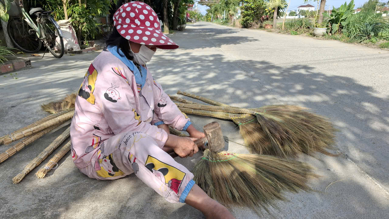 Trước khi “làm đẹp” chổi, phụ nữ cầm búa gỗ cho chổi xòe ra- Ảnh: Mạnh Trâm Trân
