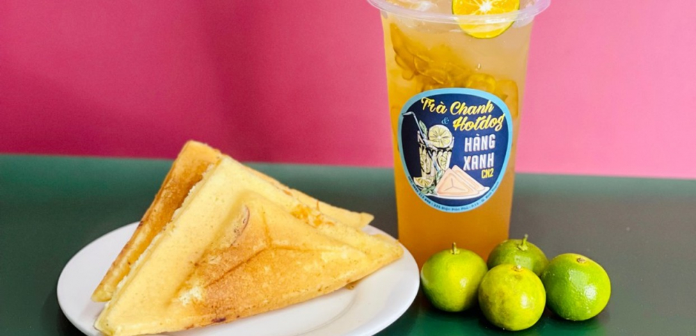 Trà Chanh và Hotdog Hàng Xanh, nằm tại 335 Điện Biên Phủ, phường 15, quận Bình Thạnh, là một điểm ăn vặt buổi tối nổi tiếng tại Sài Gòn mà nhiều bạn trẻ và sinh viên yêu thích. Quán vỉa hè này mở cửa đến khoảng 22:30–23:00 với mức giá rất phải chăng chỉ từ khoảng 5.000–10.000 đồng cho từng phần hotdog cùng các món ăn nhẹ khác, kèm theo nhiều lựa chọn nước giải khát mát lạnh như trà chanh đặc trưng. Hotdog ở đây được chuẩn bị nóng hổi, thơm phức với lớp nhân phong phú, tạo nên hương vị giản dị nhưng cuốn hút. Không gian ngồi ghế nhựa ven đường cùng không khí sôi động về đêm khiến địa điểm này trở thành nơi tụ tập bạn bè lý tưởng sau giờ học hay làm việc.
