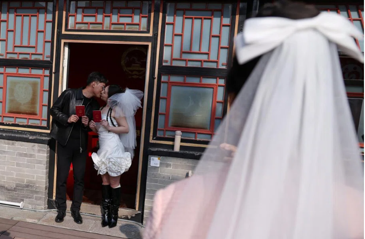 Một cặp vợ chồng mới cưới chụp ảnh với giấy đăng ký kết hôn sau khi họ đăng ký tại Chùa Huguo Guanyin, ở Bắc Kinh, Trung Quốc, ngày 28 tháng 10 năm 2025. REUTERS/Tingshu Wang