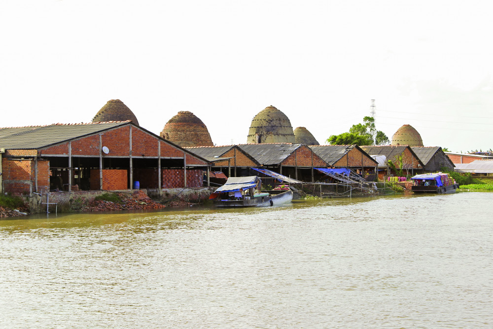 Nằm nép mình bên kênh Thầy Cai, ven dòng Cổ Chiên hiền hòa, làng gốm đỏ Vĩnh Long hình thành từ đầu thế kỷ XX, từng là một trong những trung tâm sản xuất gạch, gốm sầm uất bậc nhất miền Tây. Những lò gốm hình vòm cổ kính, nhuốm màu đỏ nung trầm mặc, xếp san sát nhau qua năm tháng, tạo nên khung cảnh như một “vương quốc” của đất và lửa giữa miền sông nước – nơi thời gian dường như trôi chậm hơn.