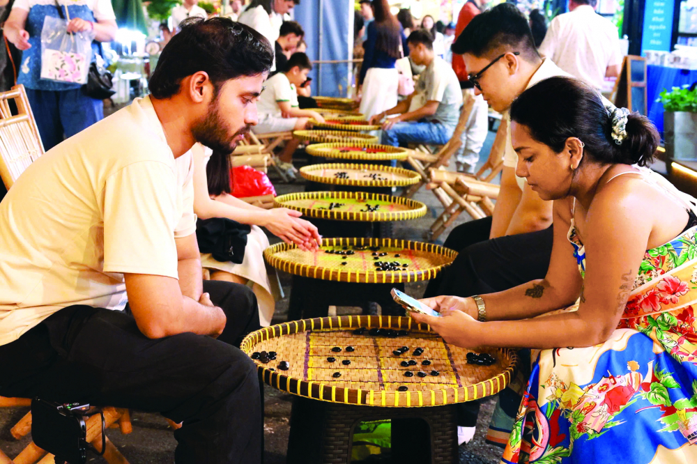 Du khách nước ngoài trải nghiệm trò chơi  ô ăn quan tại ngày hội Sách và Văn hóa đêm  tại Đường sách TPHCM - ẢNH: HỒNG NGA