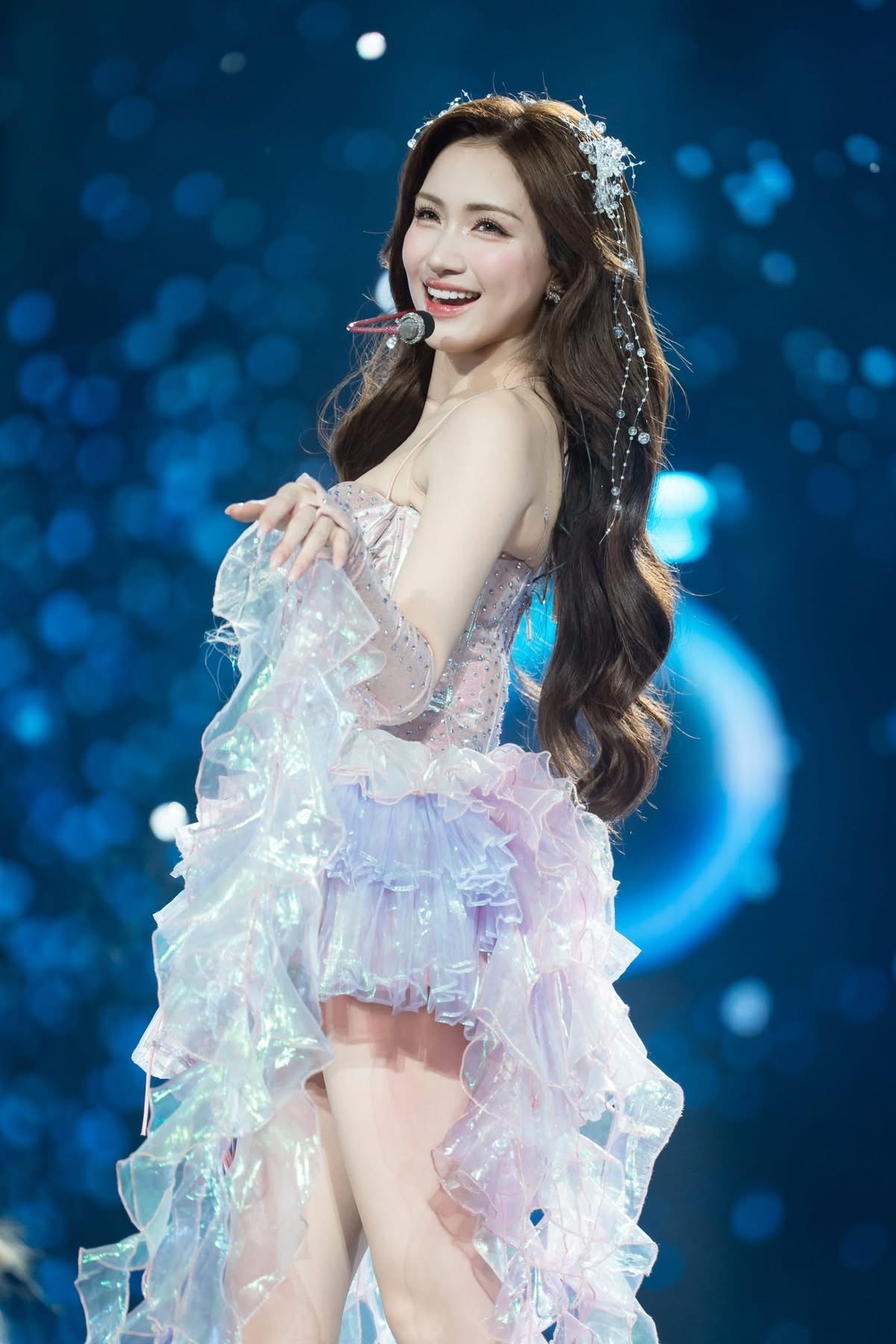 Về trang điểm, Hòa Minzy chọn phong cách trong trẻo với làn da sáng mịn, má hồng nhẹ, môi hồng bóng và đôi mắt được nhấn vừa phải, giúp gương mặt rạng rỡ, tươi tắn dưới ánh đèn sân khấu, hài hòa với tổng thể trang phục.