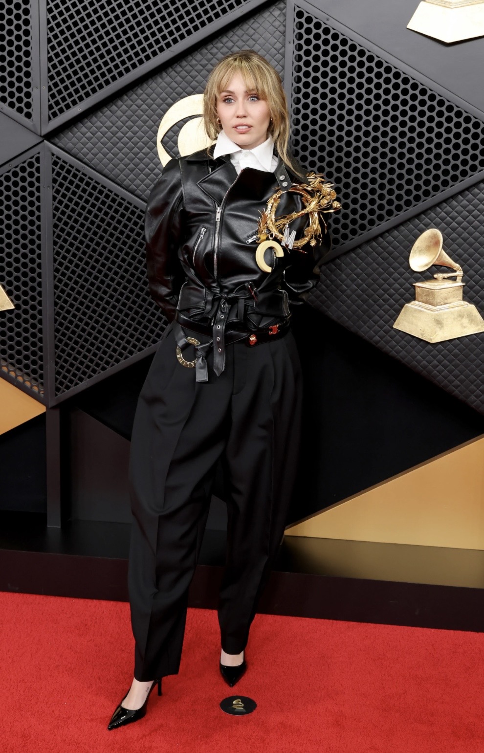 Miley Cyrus ghi điểm với phong cách cá tính và mạnh mẽ, mang đậm tinh thần rock-chic hiện đại. Áo khoác da đen dáng biker kết hợp sơ mi trắng cổ đứng tạo nên sự đối lập thú vị giữa nổi loạn và thanh lịch. Quần đen dáng suông cùng giày cao gót mũi nhọn giúp tổng thể gọn gàng, sắc sảo. 