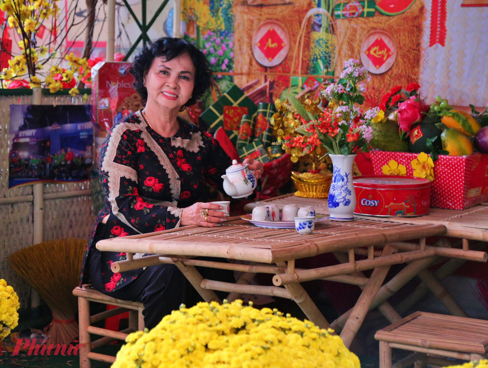 Phông nền phía sau được trang trí bằng câu đối đỏ, đèn lồng, họa tiết hoa mai, hoa đào và chữ “Tết” cách điệu, tạo thành góc “check-in” ấm cúng, hoài niệm.