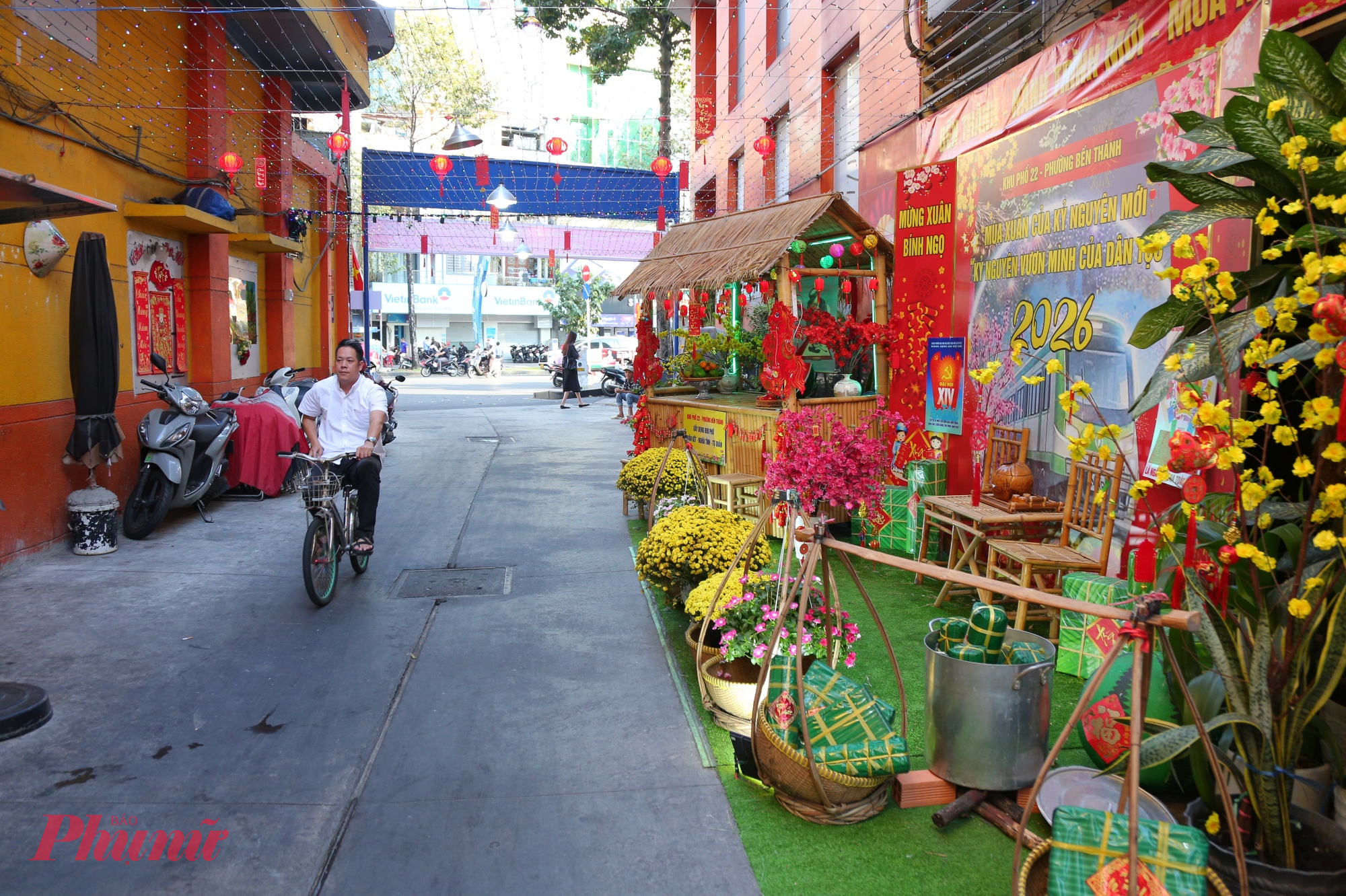 Dọc con hẻm 100 Trần Hưng Đạo là những dây cờ đỏ sao vàng được treo xen kẽ trên cao, kết hợp cùng đèn lồng đỏ và đèn trang trí, khiến không gian vừa rực rỡ sắc xuân vừa trang nghiêm, đậm tinh thần cộng đồng.