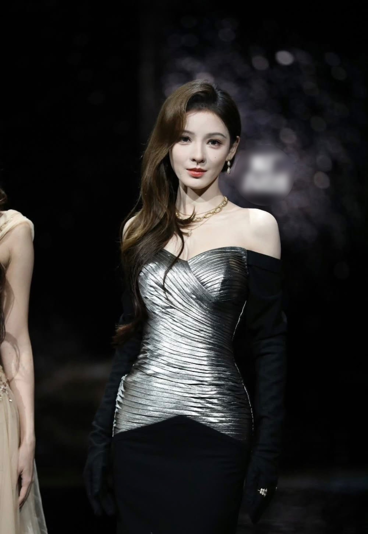 Trương Hinh Dư gây chú ý với váy ánh bạc trễ vai, thiết kế xếp nếp chạy dọc thân váy tạo hiệu ứng thị giác mạnh mẽ. Khoác hờ găng tay đen, bộ trang phục mang tinh thần haute couture, kết hợp hài hòa giữa vẻ sắc sảo hiện đại và sự mềm mại nữ tính.