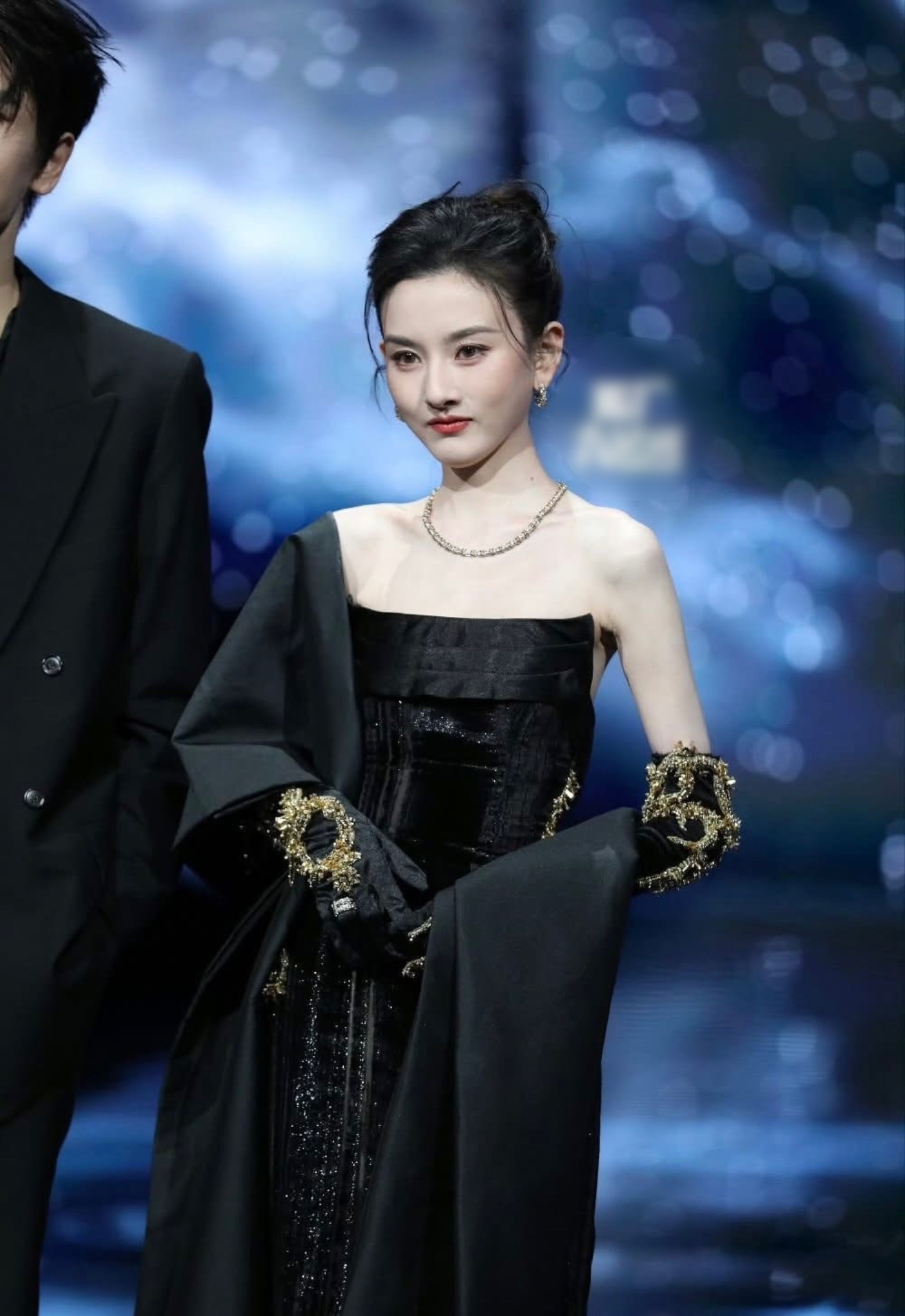 Vẫn là gam đen nhưng được xử lý theo hướng tối giản, Tống Tổ Nhi chọn váy cúp ngực kết hợp áo choàng rời. Chi tiết đính kết ánh vàng ở găng tay tạo điểm nhấn ấn tượng, khẳng định xu hướng đơn giản nhưng tinh tế trên thảm đỏ sự kiện.