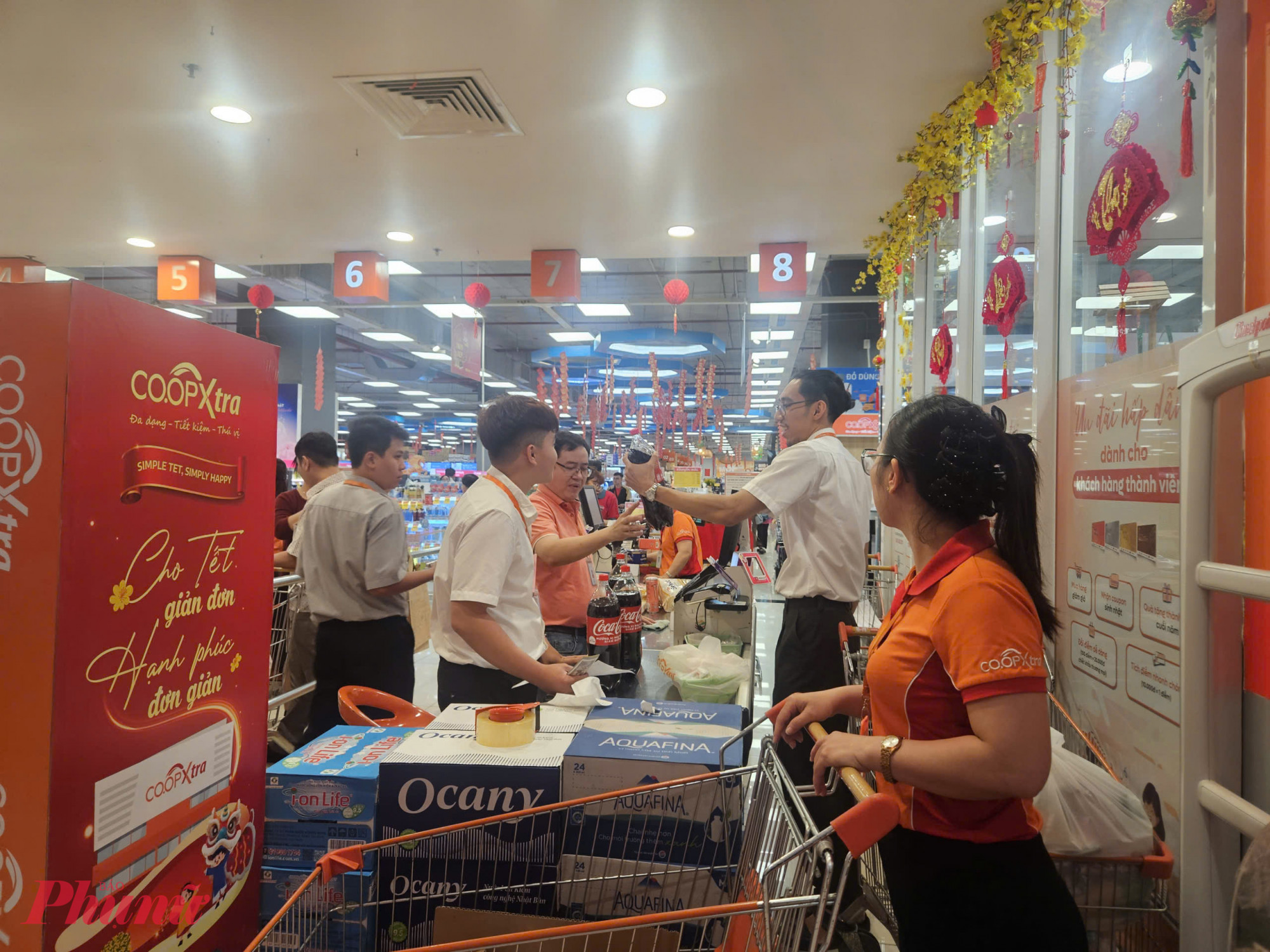 Khu vực quầy thanh toán tại một siêu thị Co.opXtra ở TPHCM đông kín khách trong ngày cao điểm mua sắm cận tết. Xe đẩy xếp hàng chờ tính tiền, nhiều giỏ hàng đầy ắp nước giải khát, thùng nước suối, bánh kẹo và nhu yếu phẩm. Nhân viên thu ngân làm việc liên tục, phối hợp phân luồng để giảm thời gian chờ.