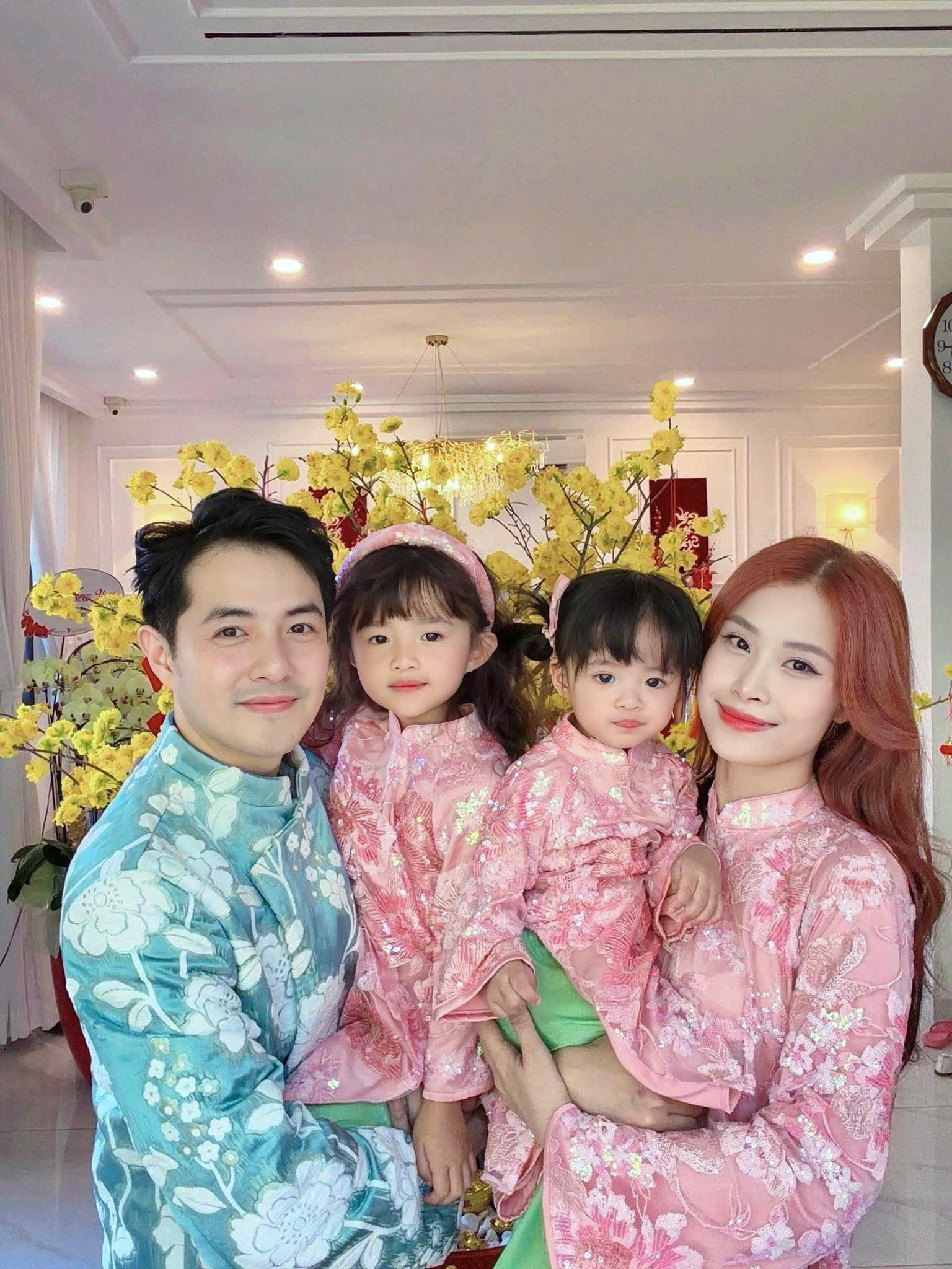 Hai bé gái nhà Đông Nhi - Ông Cao Thắng xuất hiện đáng yêu trong những thiết kế áo dài hồng pastel đồng điệu. Cả 2 cùng diện áo dài cách tân chất liệu ánh nhũ nhẹ, phủ họa tiết hoa thêu tinh xảo, tạo cảm giác mềm mại, trong trẻo. Phom dáng rộng rãi giúp các bé thoải mái vận động, trong khi phần cổ đứng và tay áo truyền thống vẫn giữ trọn nét Á Đông. Sự đồng bộ về màu sắc và chất liệu không chỉ khiến hai chị em trông xinh xắn như bản sao thu nhỏcủa nhau, mà còn mang đến tổng thể hài hòa, ấm áp và đậm không khí gia đình trong những ngày đầu năm.