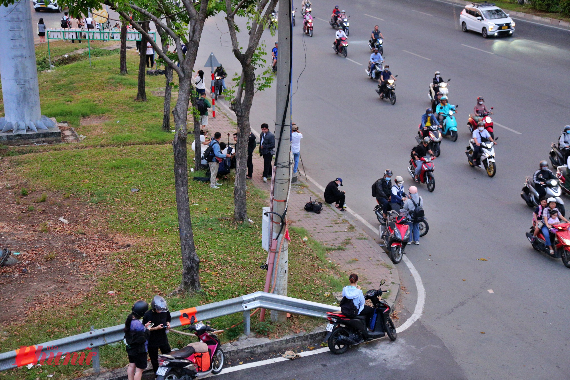 Không chỉ trên cầu đi bộ, dưới vỉa hè và dọc lề đường Võ Nguyên Giáp, nhiều người cũng kiên nhẫn chờ đợi, mắt hướng về phía chân trời nơi mặt trời dần hạ thấp phía sau cầu Sài Gòn.