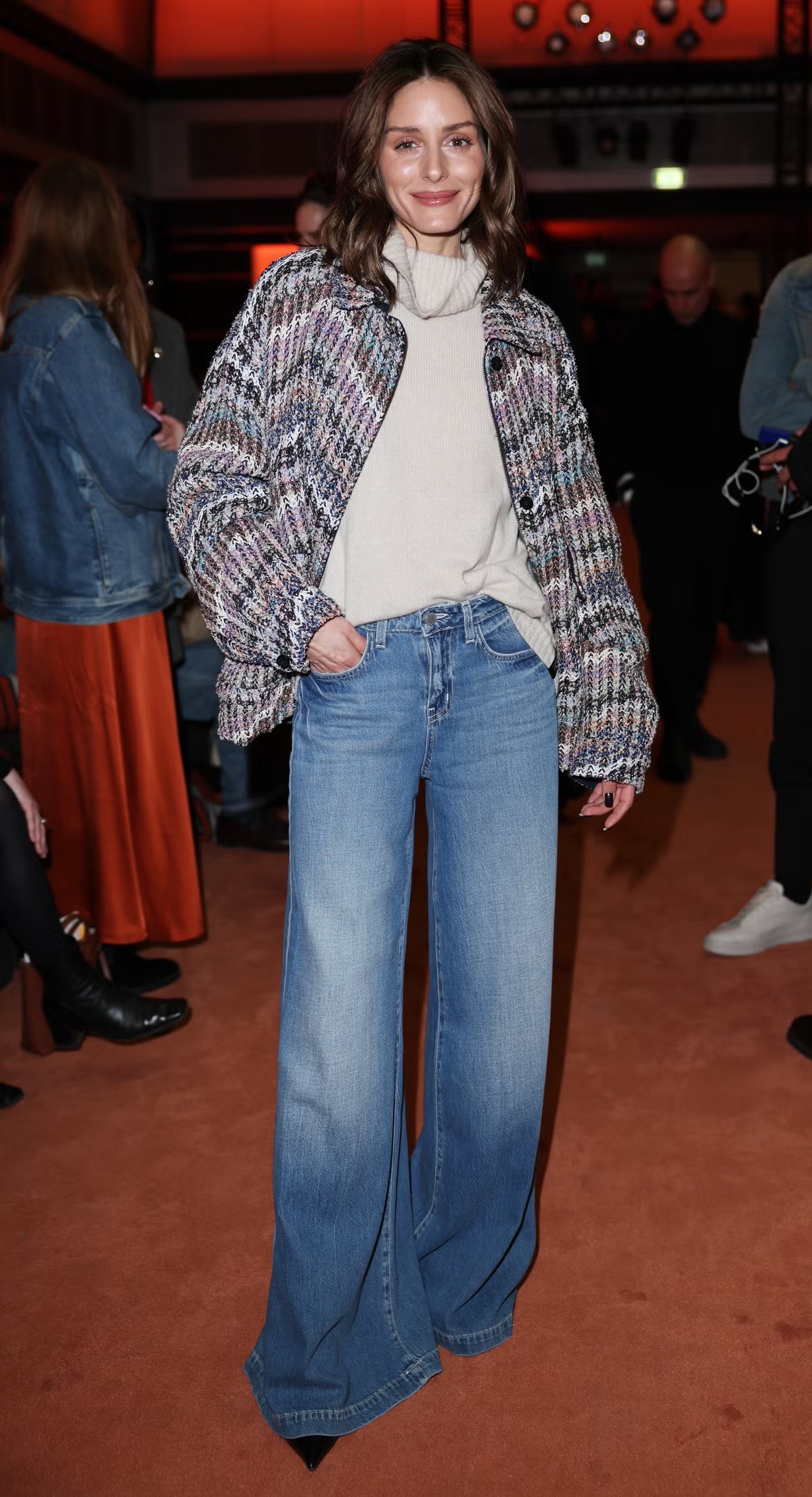 Tại show diễn của nhà mốt Missoni, Olivia Palermo mang đến hình ảnh thanh lịch khi lựa chọn áo len cổ lọ màu kem mềm mại, kết hợp cùng áo khoác dệt kim họa tiết zigzag, tạo nên hiệu ứng màu sắc tinh tế nhưng không phô trương. Quần jeans ống rộng cạp cao giúp tổng thể thêm phần phóng khoáng, hiện đại. Cách phối phụ kiện tối giản và mái tóc uốn nhẹ tự nhiên càng tôn lên vẻ sang trọng nhẹ nhàng của người đẹp.