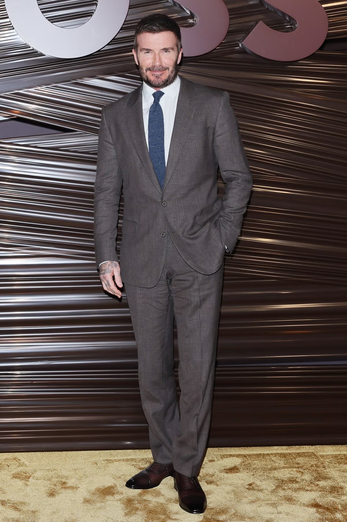 Góp mặt tại show Boss tại Tuần lễ thời trang Milan 2026, David Beckham tiếp tục khẳng định vị thế biểu tượng phong cách nam giới với diện mạo lịch lãm, chuẩn mực và đầy bản lĩnh. Anh lựa chọn bộ vest màu nâu xám phom dáng cổ điển, được cắt may sắc sảo. Áo sơ mi trắng kết hợp cà vạt xanh trầm tạo điểm nhấn tinh tế, mang đến sự cân bằng giữa nét truyền thống và tinh thần đương đại.