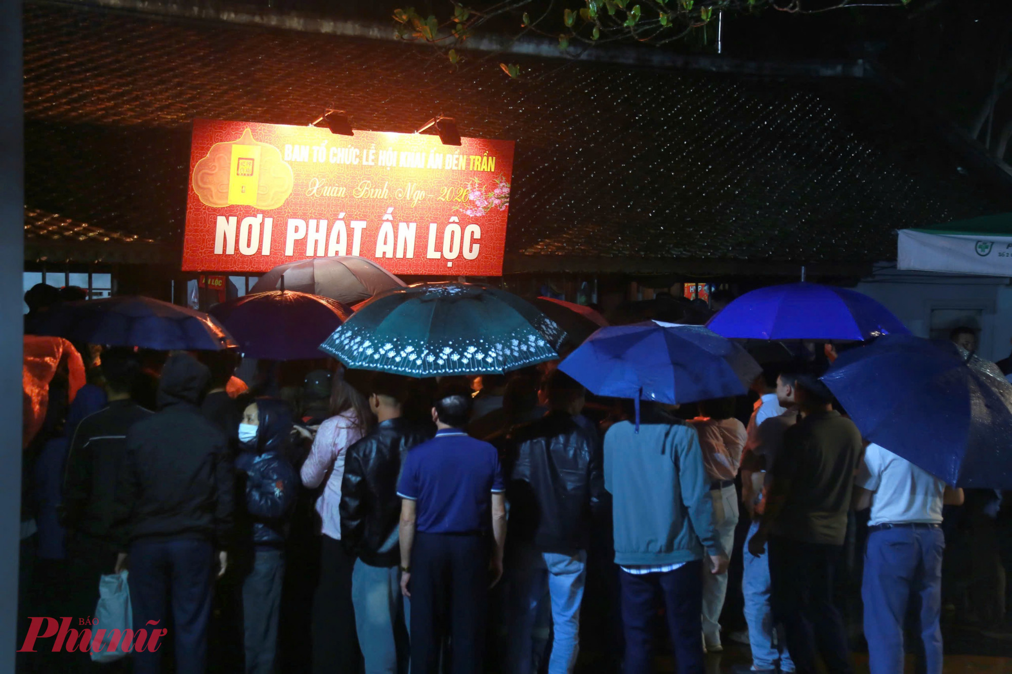 Dòng người kéo dài qua nhiều lối đi quanh khuôn viên đền. Dưới ánh đèn, những chiếc ô đủ màu tạo nên khung cảnh đặc biệt của buổi phát ấn rạng sáng.