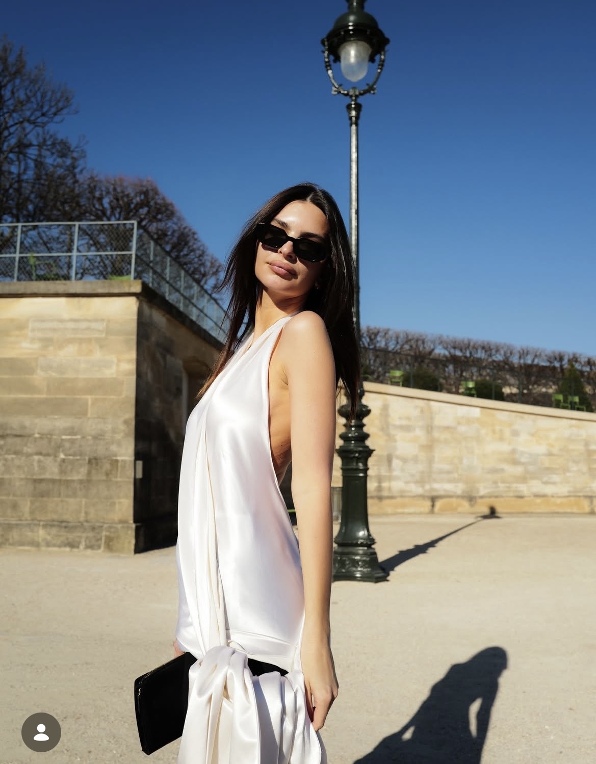 Emily Ratajkowski mang đến phong cách tối giản nhưng gợi cảm khi diện thiết kế váy lụa trắng dáng suông với đường cắt sâu ở phần hông, vừa phô diễn vóc dáng mềm mại vừa giữ được nét thanh lịch. Chất liệu satin rủ nhẹ tạo hiệu ứng mềm mại, uyển chuyển. Cô kết hợp phụ kiện kính râm đen bản nhỏ và clutch tối màu hài hoà. Mái tóc xõa thẳng tự nhiên cùng lối trang điểm tối giản giúp Emily Ratatkowski thu hút mọi ánh nhìn khi sải bước tại show diễn Dior 2026.