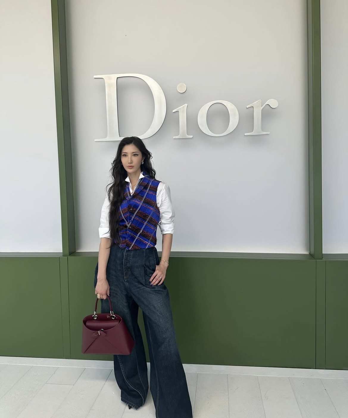 Ca sĩ Hàn Quốc Ejae xuất hiện với phong cách thanh lịch pha nét menswear hiện đại. Cô phối áo sơ mi trắng cổ điển cùng gilet họa tiết kẻ xanh - đỏ, tạo điểm nhấn cho phong cách thời thượng chuẩn tinh thần Dior. Quần denim ống rộng dáng suông giúp tổng thể trở nên phóng khoáng, cân bằng hoàn hảo giữa sự chỉn chu và thoải mái.