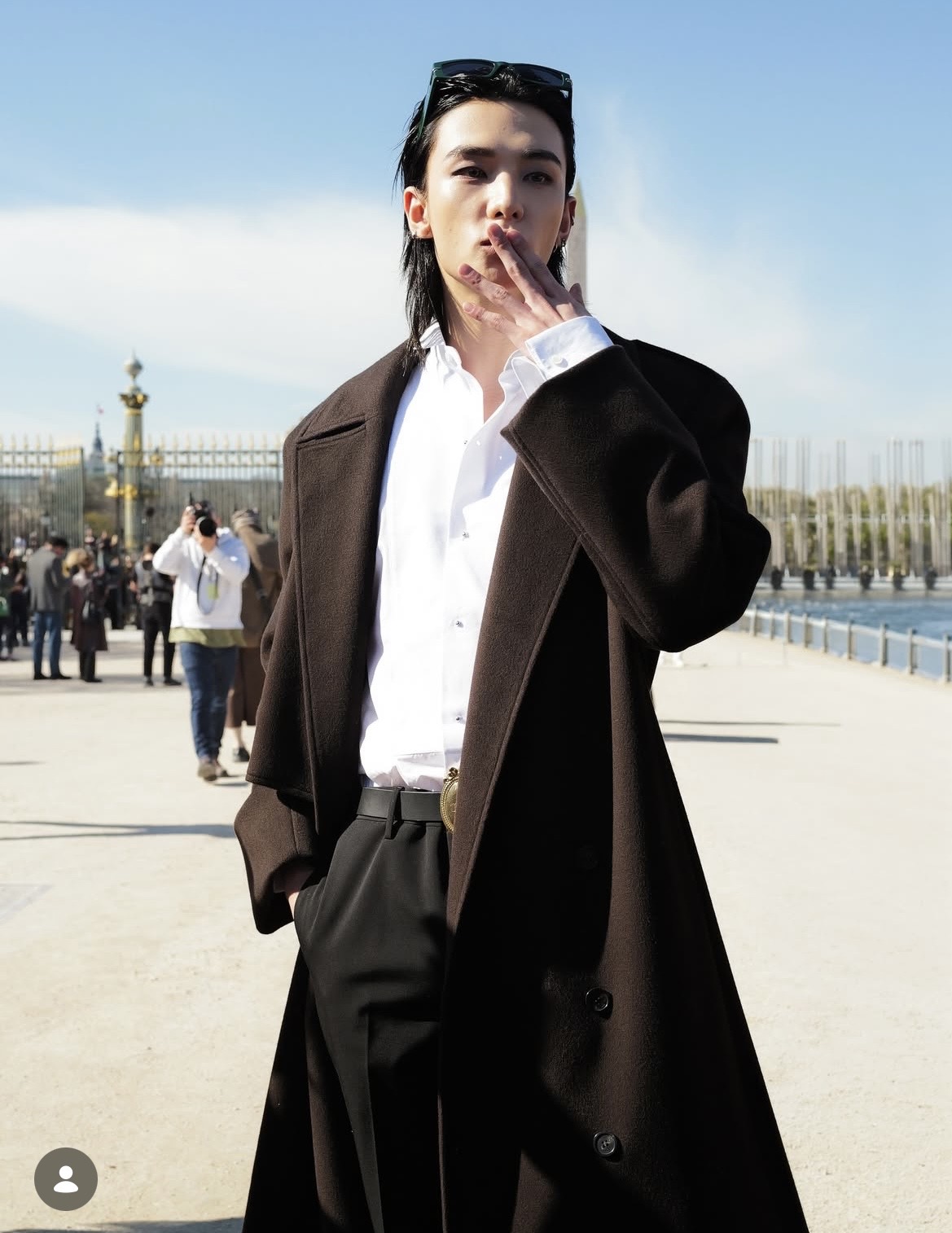 Hyun Jin (Stray Kids) lựa chọn áo sơ mi trắng phom rộng phối cùng quần tây đen cạp cao và khoác ngoài trench coat dáng dài màu nâu sẫm để hoàn thiện phong cách lịch lãm, tối giản. Cách sơ vin gọn gàng, thắt lưng bản vừa cùng khuy áo mở nhẹ giúp tổng thể vừa chỉn chu vừa phóng khoáng. Phụ kiện kính mát đặt trên đầu và kiểu tóc dài chải ngược càng nhấn mạnh khí chất nghệ sĩ, lạnh lùng nhưng cuốn hút. 