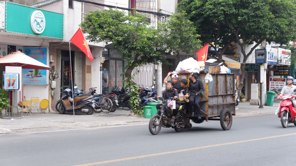 4 người ngồi trên xe lôi tự chế, kéo theo thùng rác phía sau không đội mũ bảo hiểm. Ảnh ghi nhận trên đường Chu Văn An, quận Bình Thạnh cũ.