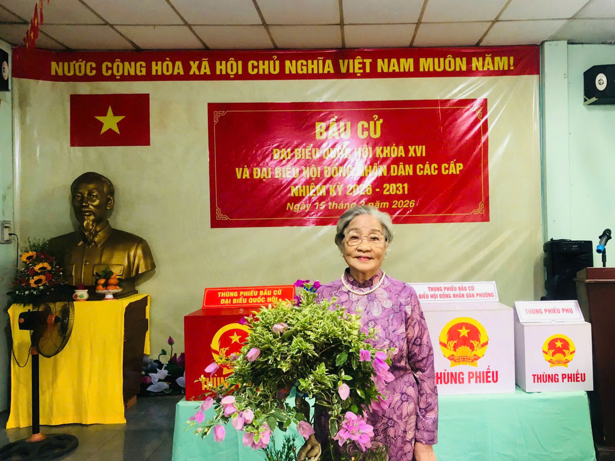 Sáng nay, mẹ dậy rất sớm, mặc bộ áo dài tím yêu thích và trang điểm nhẹ cho tươi tắn