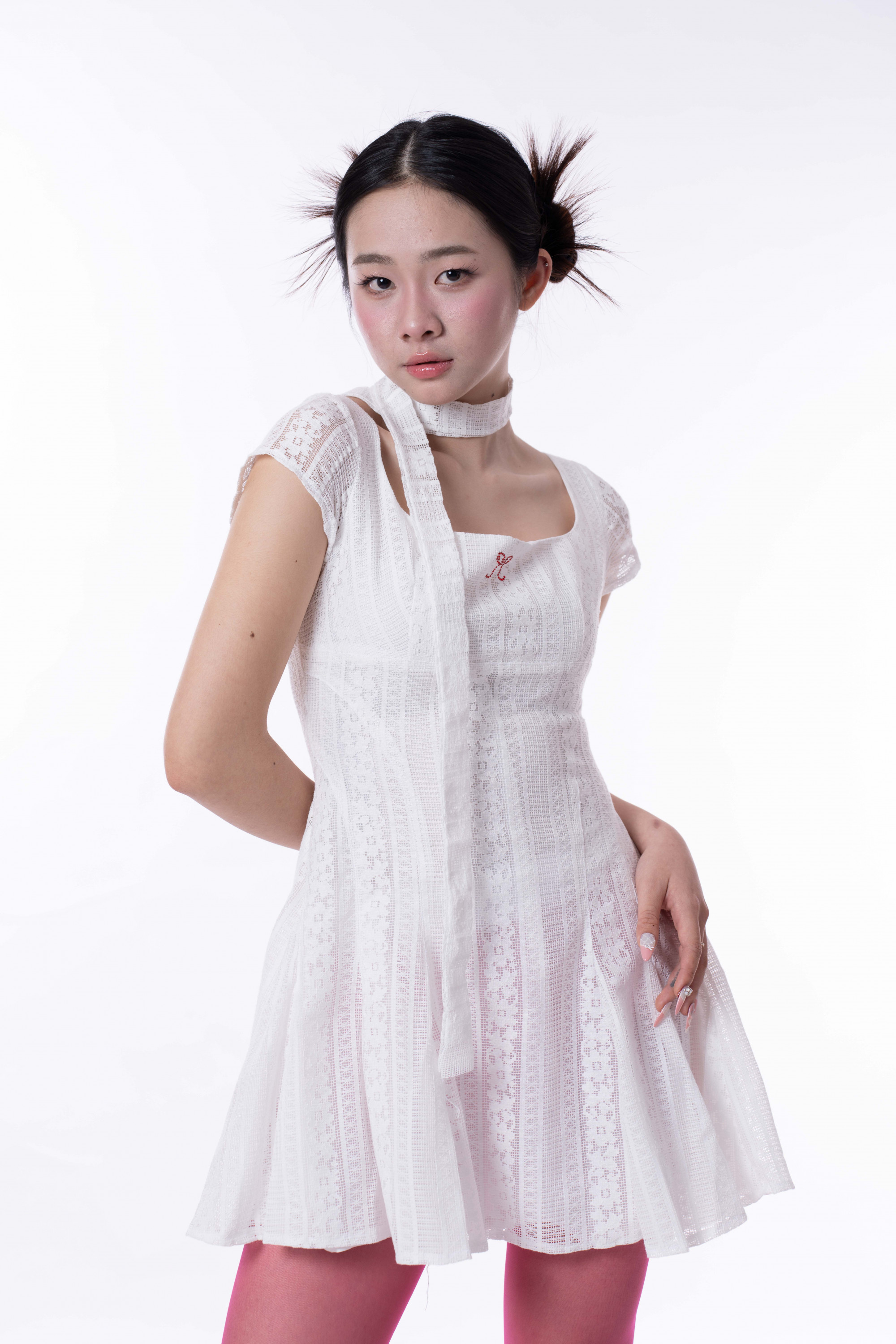 Chiếc váy trắng chất liệu ren mỏng mang lại cảm giác nhẹ nhàng, thiết kế cổ quấn và phom váy xòe giúp tôn lên vóc dáng thanh mảnh của Kiều Diễm. Điểm nhấn nằm ở cách phối cùng tất hồng nổi bật và kiểu tóc buộc 2 bên cá tính, tạo nên sự đối lập thú vị giữa vẻ dịu dàng và tinh thần trẻ trung, sáng tạo. 