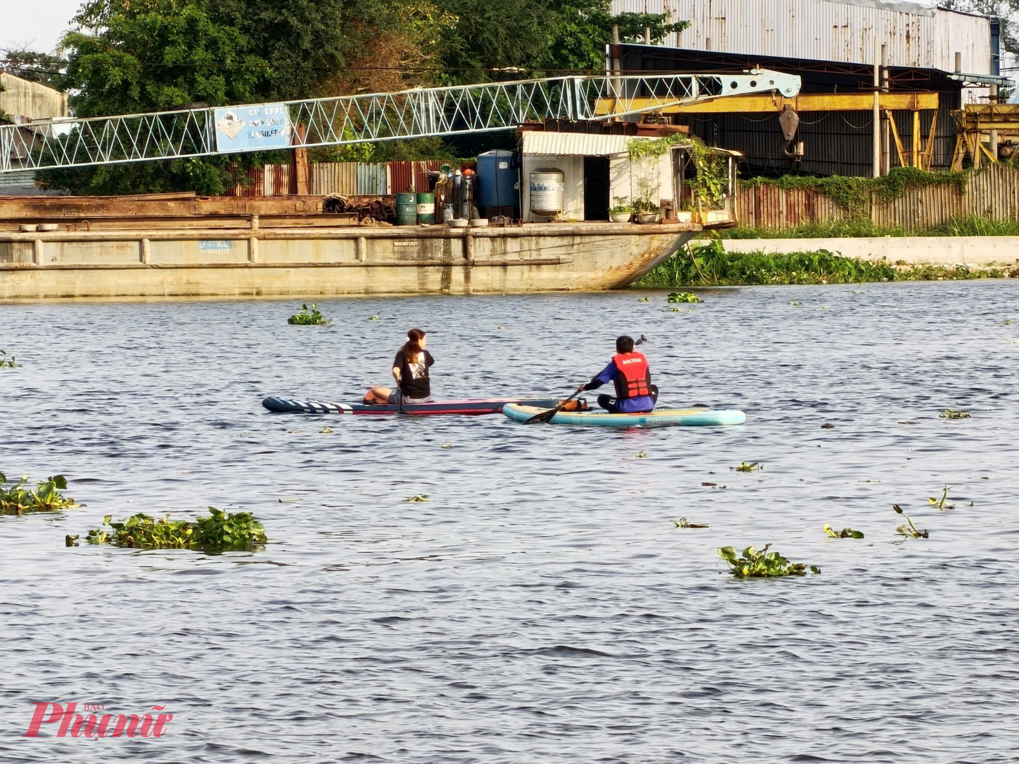 Một cô gái không mặc áo phao vừa chèo SUP vừa quay lại quan sát một chiếc sà lan đang dần tới - Ảnh: Nguyễn Văn
