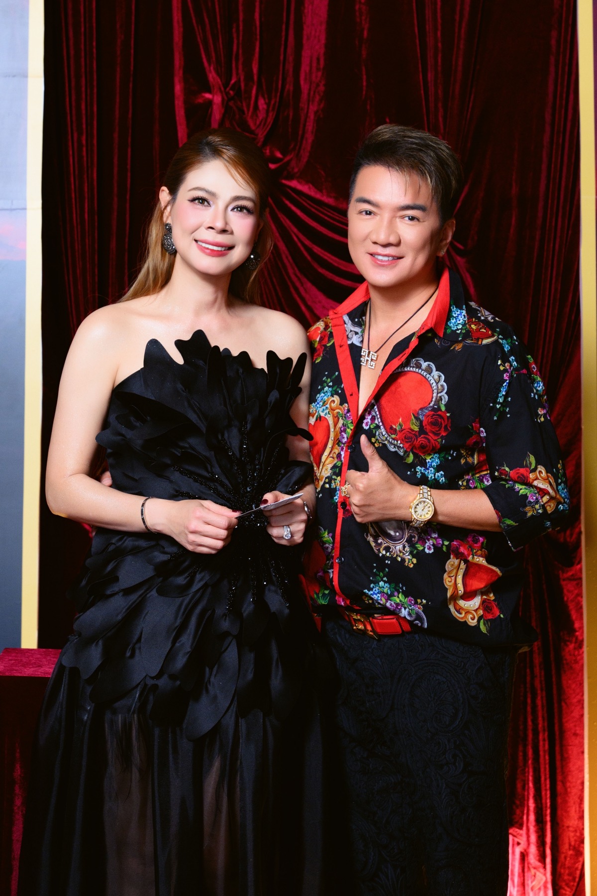 Ca sĩ Đàm Vĩnh Hưng đến chung vui dịp sinh nhật của Thanh Thảo. Anh lựa chọn áo sơ mi họa tiết cầu kỳ với gam màu đen - đỏ chủ đạo, điểm xuyết những hình in hoa và chi tiết cầu kỳ tạo cảm giác vừa sang trọng vừa phá cách. Phần cổ áo mở nhẹ kết hợp dây chuyền bản lớn giúp tổng thể thêm phần phóng khoáng. 