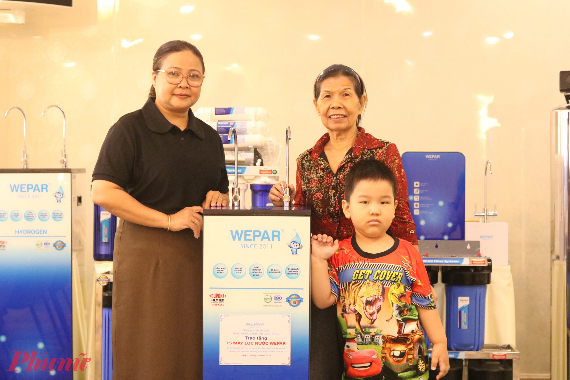 Bà Nguyễn Thị Minh Hậu – Phó chủ tịch Ủy ban MTTQ Việt Nam phường Bình Hưng Hòa, Chủ tịch Hội LHPN phường (bìa trái) – trao máy lọc nước cho bà Vũ Thị Lan – 64 tuổi, ở khu phố 62, phường Bình Hưng Hòa. Bà Lan đang chăm sóc 2 cháu ngoại còn nhỏ tuổi. Mẹ của các em mất do COVID – 19 vào năm 2021. Đến năm 2022, cha của các em cũng ra đi vì đột quỵ - Ảnh: Mẫn Nhi