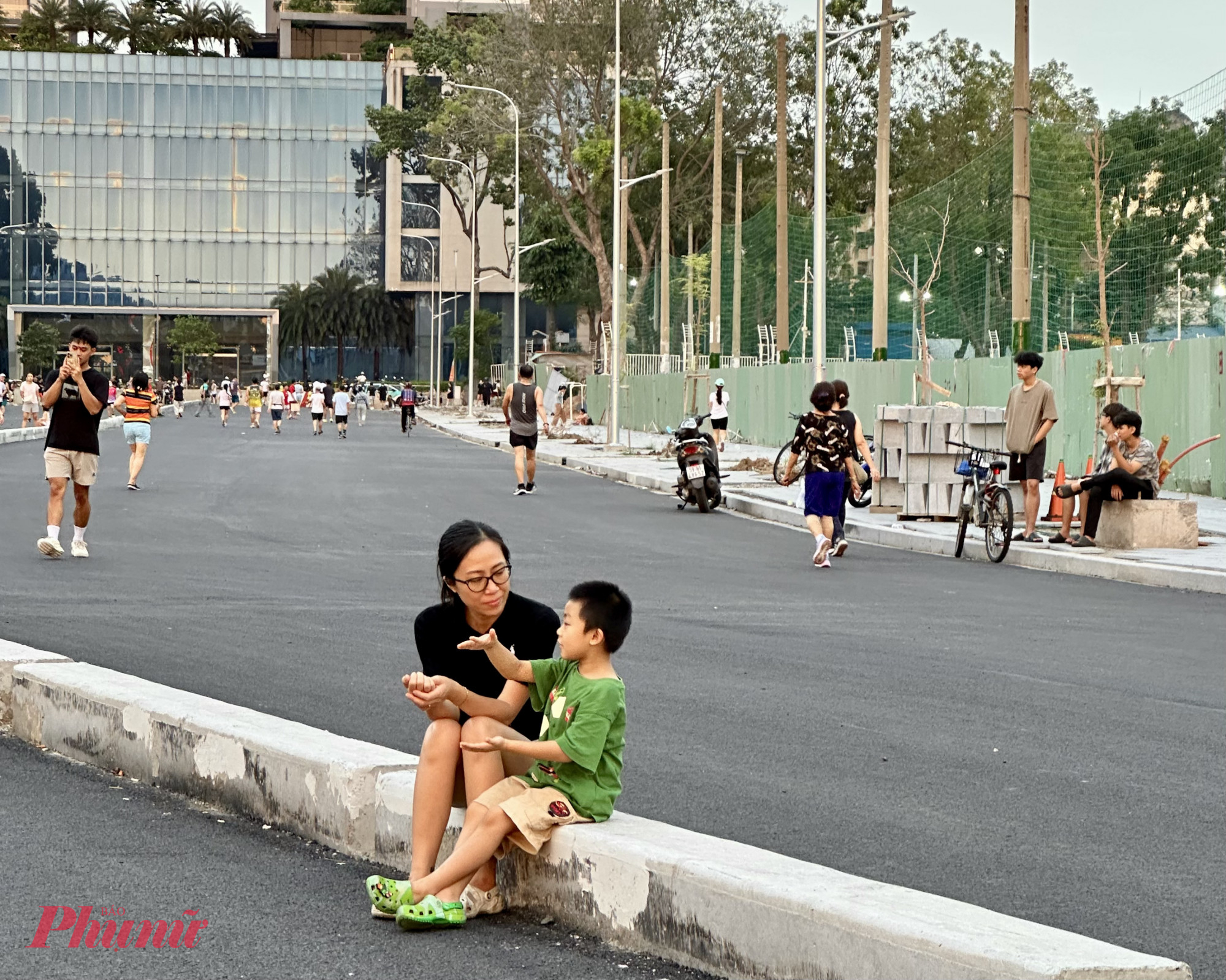 Hai mẹ con ngồi trên dãi phân cách, chuyện trò giản dị mà ấm áp – như thể nơi này vốn dĩ đã là một góc quen của khu phố.