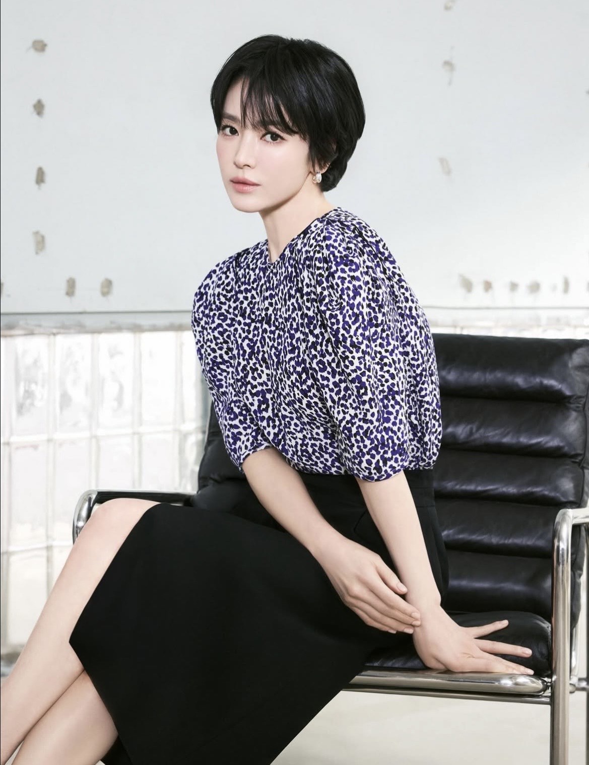 Song Hye Kyo trong bức ảnh này toát lên vẻ thanh lịch, tinh tế và tối giản đặc trưng. Cô lựa chọn một chiếc áo họa tiết nhẹ nhàng với phom dáng tay phồng, tạo điểm nhấn mềm mại và nữ tính, kết hợp cùng chân váy đen dáng dài đơn giản giúp tổng thể trở nên cân đối và sang trọng. Bảng màu trung tính pha chút họa tiết giúp cô vừa nổi bật vừa giữ được nét nhã nhặn. Kiểu tóc ngắn ôm gọn khuôn mặt cùng lớp trang điểm tự nhiên càng làm tôn lên vẻ đẹp dịu dàng, hiện đại. Tổng thể, trang phục của cô thể hiện gu thẩm mỹ tinh giản nhưng vẫn đầy cuốn hút và đẳng cấp.