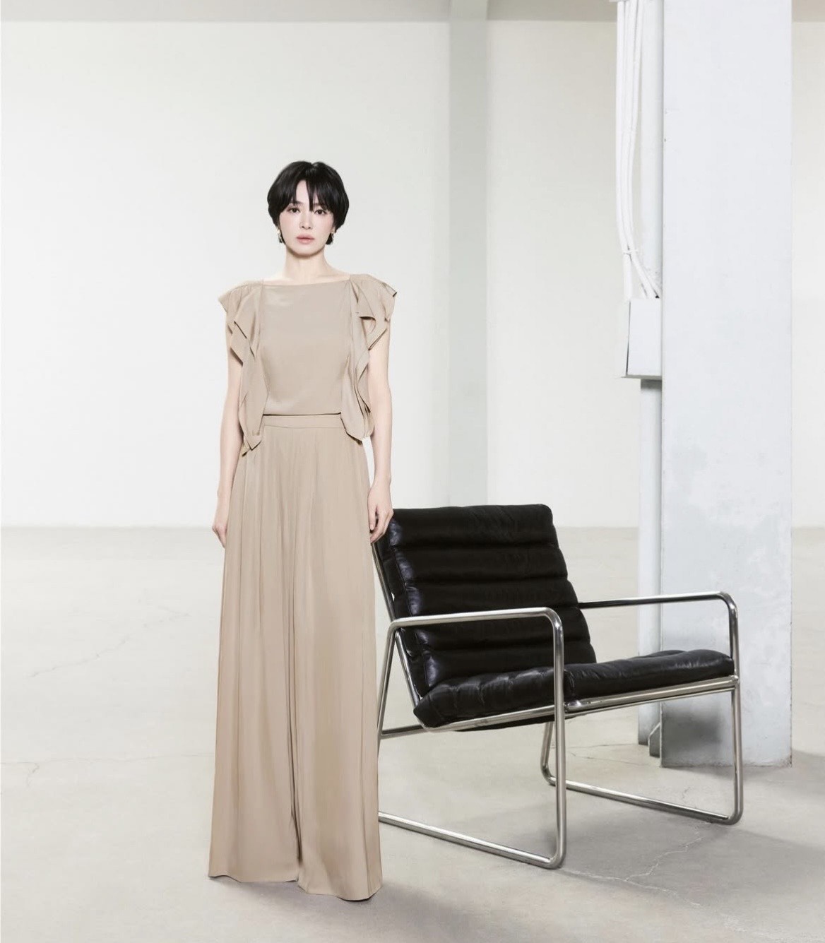 Bộ trang phục tông be gồm áo blouse và chân váy dài mang đến vẻ ngoài trang nhã, phù hợp với những môi trường làm việc yêu cầu tính chuyên nghiệp cao. Chất liệu mềm mại, bay nhẹ giúp giảm cảm giác nặng nề trong mùa hè. Song Hye-kyo chọn lối trang điểm tông nude ấm, nhấn nhẹ vào mắt và môi, tạo cảm giác hài hòa, sang trọng.