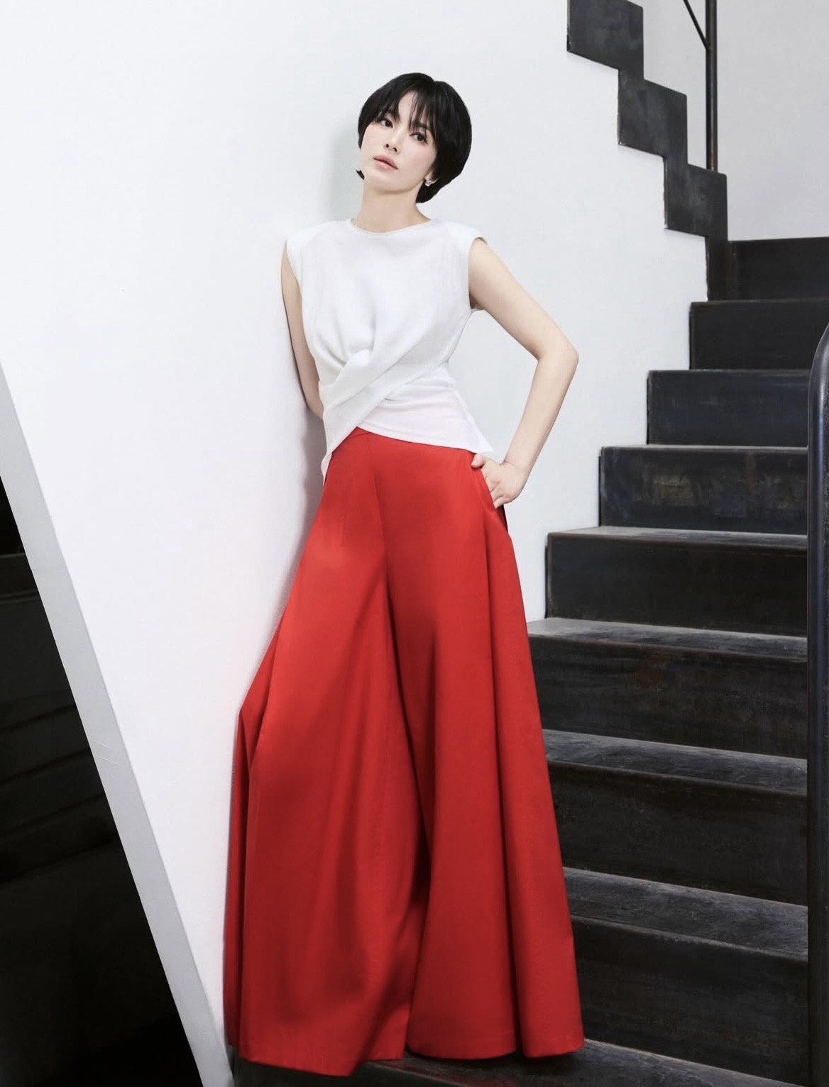 Ở một lựa chọn khác, nữ diễn viên kết hợp áo trắng sát nách với chân váy đỏ dáng dài. Sự tương phản giữa hai gam màu tạo hiệu ứng thị giác mạnh mẽ nhưng không quá chói mắt. Kiểu tóc ngắn ôm gọn gương mặt cùng lớp makeup tự nhiên – tập trung vào làn da mịn và môi hồng nhẹ – giúp cân bằng tổng thể, giữ được nét thanh lịch cần có trong môi trường công sở.