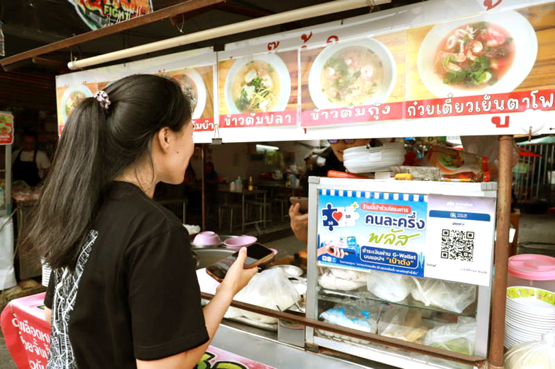 Một phụ nữ dùng ứng dụng di động để thanh toán cho người bán hàng rong theo chương trình hỗ trợ chi trả Khon La Khrueng Plus của Chính phủ Thái Lan tại chợ Pak Nam, tỉnh Samut Prakan vào tháng 10/2025. Chương trình này dự kiến được tái khởi động vào tháng 4/2026 - ẢNH: SOMCHAI POOMLARD (Bangkok Post)