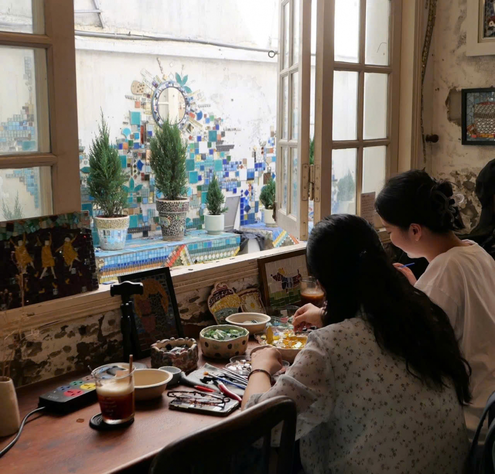 Toòng Teng Mosaic (412/10 Nơ Trang Long, Phường 13, Bình Lợi Trung) từ lâu đã rất quen thuộc với các tính đồ đam mê workshop. Giữa không gian ấm áp và bình yên của quán, bạn sẽ cảm thấy vô cùng thoải mái để thử sức với workshop làm tranh từ những viên đá đầy màu sắc. Quán cung cấp các dụng cụ khảm tranh và có nhân viên quán sẽ hướng dẫn quy trình thực hiện. Thứ tự lần lượt là chọn kích thước tranh, mẫu vẽ, màu gạch tương ứng, phác thảo mẫu lên khung, chuẩn bị đồ dùng cắt và dán gạch. Thời gian để làm một bức tranh chỉ từ 2 đến 3 tiếng. Một điểm cộng nổi bật khác là bạn sẽ không cần phải đăng ký trước mà thời gian workshop sẽ được tổ chức rất linh hoạt tùy theo lịch của khách hàng - Ảnh: Toòng Teng Mosaic