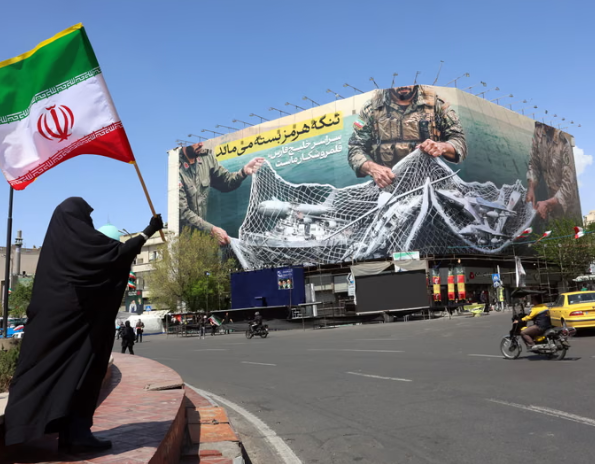 Một người phụ nữ cầm quốc kỳ Iran đứng gần một bảng quảng cáo có dòng chữ Eo biển Hormuz vẫn đóng cửa tại quảng trường Enqelab ở Tehran, ngày 5 tháng 4 năm 2026. Ảnh: AFP/Getty Images