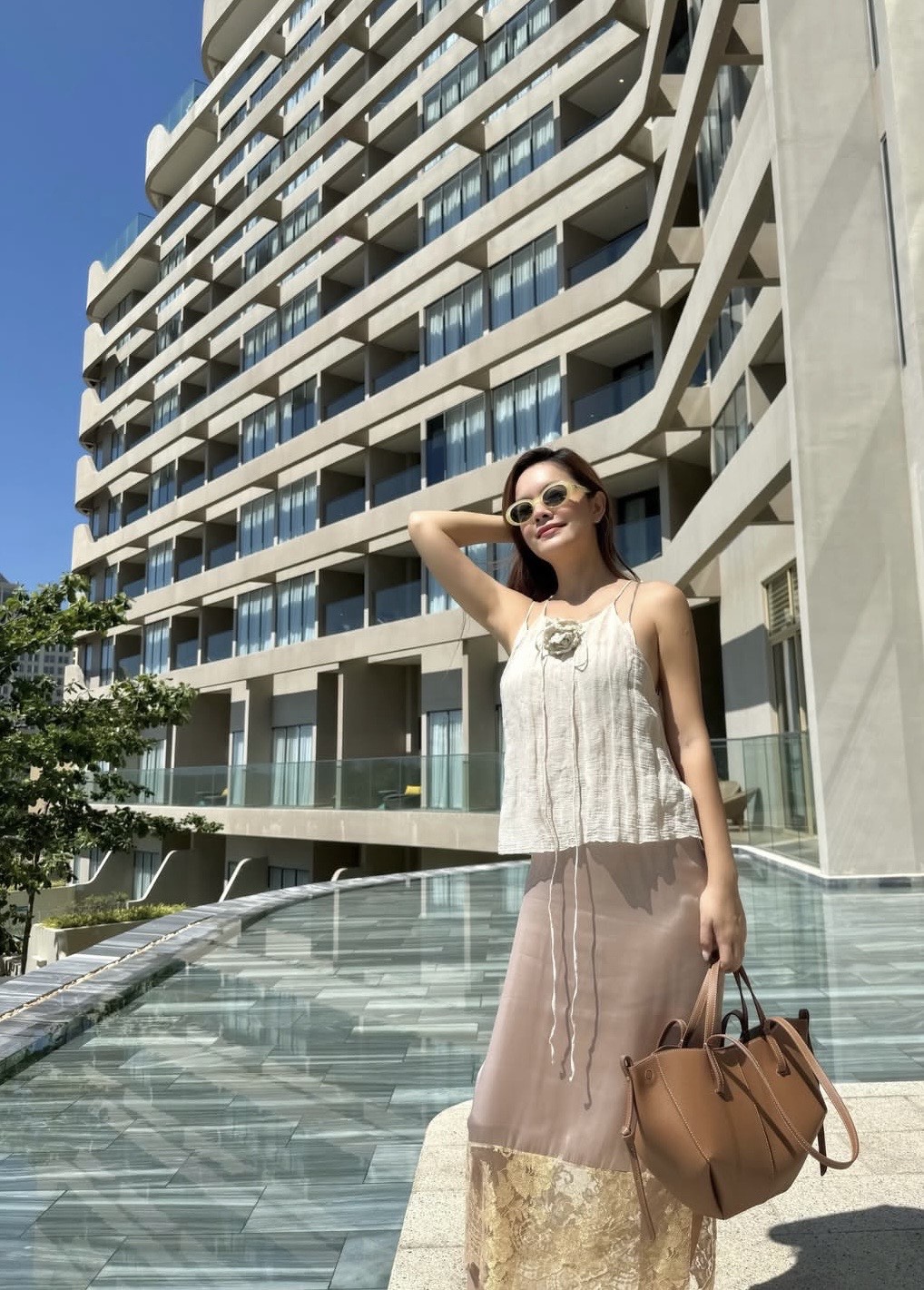 Phạm Quỳnh Anh ghi điểm với phong cách thời trang mùa hè nhẹ nhàng, nữ tính và không kém phần sang trọng tinh tế. Cô lựa chọn áo 2 dây chất liệu mỏng nhẹ, phối cùng chân váy dài gam màu trung tính với phần ren ở gấu, tạo cảm giác bay bổng và mềm mại. Bảng màu be-nude chủ đạo mang đến sự thanh lịch, phù hợp với không khí nắng hè. Phụ kiện đi kèm như túi xách da nâu cỡ lớn và kính râm sáng màu giúp tổng thể thêm phần hiện đại, đồng thời tăng tính ứng dụng cho trang phục. 