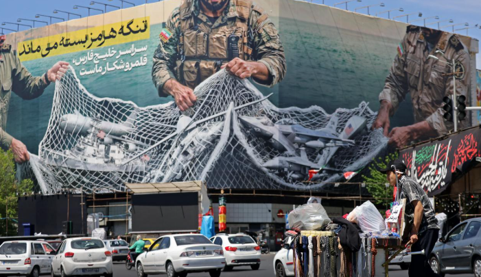 Một người bán hàng rong đẩy xe hàng của mình đi ngang qua một tấm biển khổng lồ có dòng chữ Eo biển Hormuz vẫn đóng cửa tại Quảng trường Cách mạng ở Tehran vào ngày 12 tháng 4 năm 2026. (Ảnh AFP)