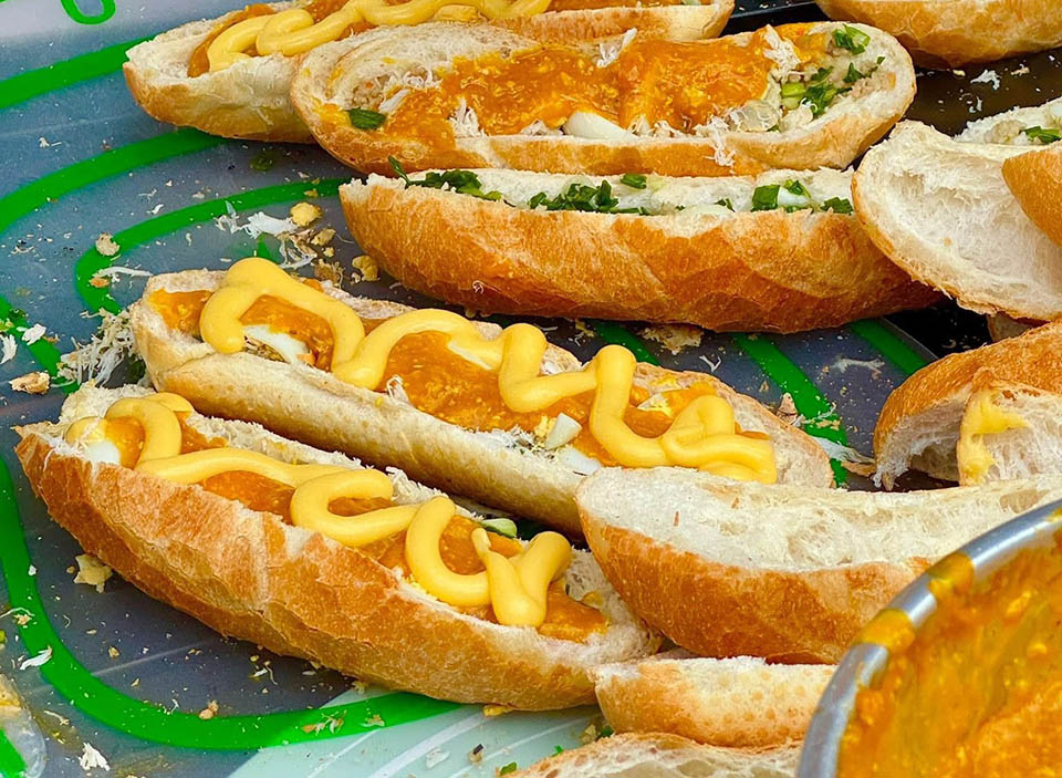 Giữa vô vàn biến tấu của bánh mì Việt, bánh mì sốt gạch cua nổi bật hơn cả nhờ hương vị đậm đà. Điều làm nên danh tiếng của bánh mì gạch cua chính là phần sốt vàng óng, sánh mịn và thơm ngậy mùi gạch cua biển. Lớp sốt này không chỉ béo ngậy mà còn đậm đà vị umami tự nhiên từ hải sản tươi sống. Khi cắn vào, thực khách sẽ cảm nhận được sự hòa quyện tuyệt vời giữa sốt gạch cua, thịt băm được nêm nếm vừa vặn, mỡ hành thơm lừng, thịt cua biển ngọt chắc và trứng cút béo bùi. Tất cả những nguyên liệu này được nướng sơ trên mai cua trước khi được cho vào ổ bánh mì.