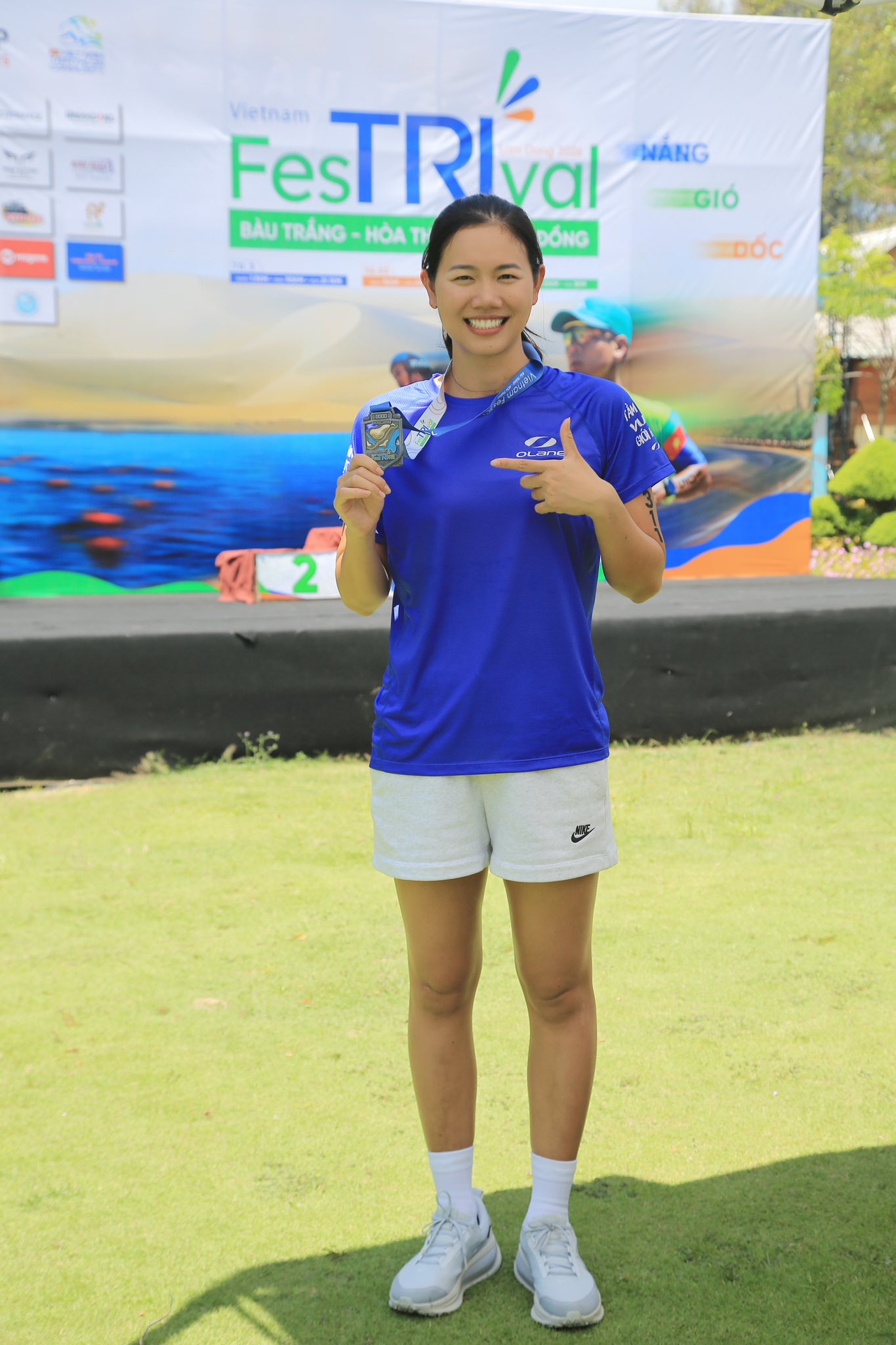 Ánh Viên khoe nụ cười tươi rói và chiếc huy chương của giải FestTRIval tại Bàu Cát. Chọn phong cách năng động và trẻ trung với chiếc áo thể thao xanh nổi bật, mái tóc tết gọn, chiếc huy chương vàng trên cổ là minh chứng cho sức mạnh của một nhà vô địch.