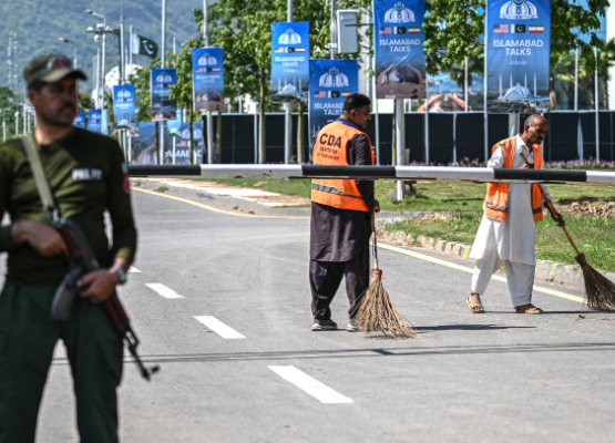 Các công nhân vệ sinh đang quét dọn một con đường trong khi một nhân viên an ninh đứng gác gần khách sạn Serena ở Islamabad vào ngày 19 tháng 4 năm 2026. (Ảnh AFP)