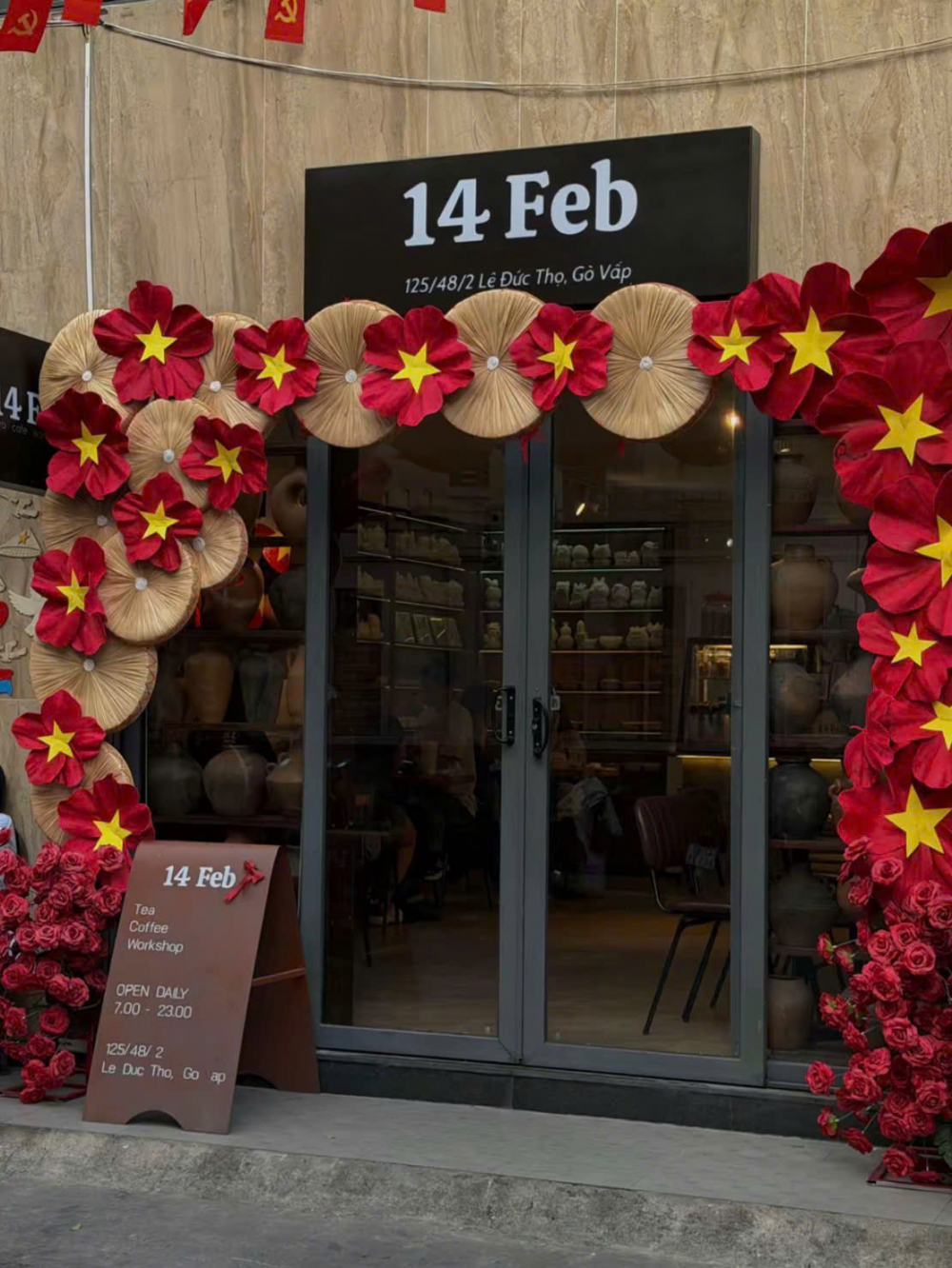 Quán 14 Feb (125/48/2 Lê Đức Thọ, phường Gò Vấp) gây ấn tượng ngay từ cái nhìn đầu tiên với mặt tiền được phủ kín sắc đỏ rực rỡ – gam màu gợi nhắc trực tiếp đến không khí thiêng liêng của ngày 30/4. Những cụm hoa hồng được sắp đặt dày đặc, đan xen tinh tế cùng hình ảnh lá cờ đỏ sao vàng được cách điệu thành một “bông hoa” lớn, tạo nên điểm nhấn thị giác vừa mềm mại vừa giàu tính biểu tượng. Tổng thể không gian bên ngoài không chỉ thu hút người qua đường mà còn gợi lên cảm giác tự hào, gần gũi, như một lời chào đầy cảm xúc hướng về ngày lễ lịch sử.