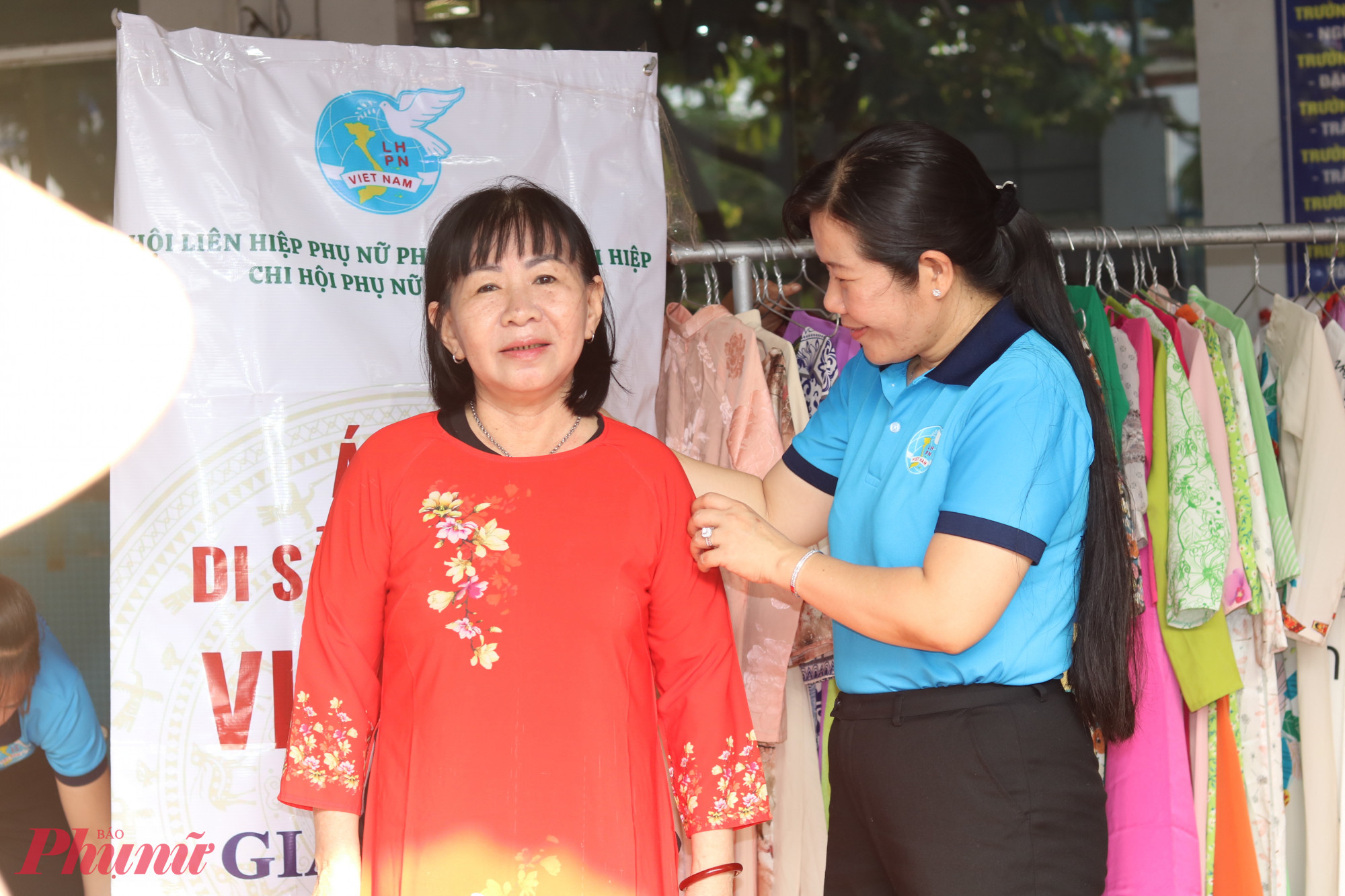 Bà Phạm Thị Mộng Hằng – Phó chủ tịch thường trực Ủy ban MTTQ Việt Nam phường Tân Thới Hiệp, Chủ tịch Hội LHPN phường (bìa phải) – giúp chị Dương Thị Nết chọn 1 bộ áo dài vừa vặn. Chị Nết nói, mặc bộ áo dài đỏ này, chị cảm thấy tự tin - Ảnh: Thảo Nguyên