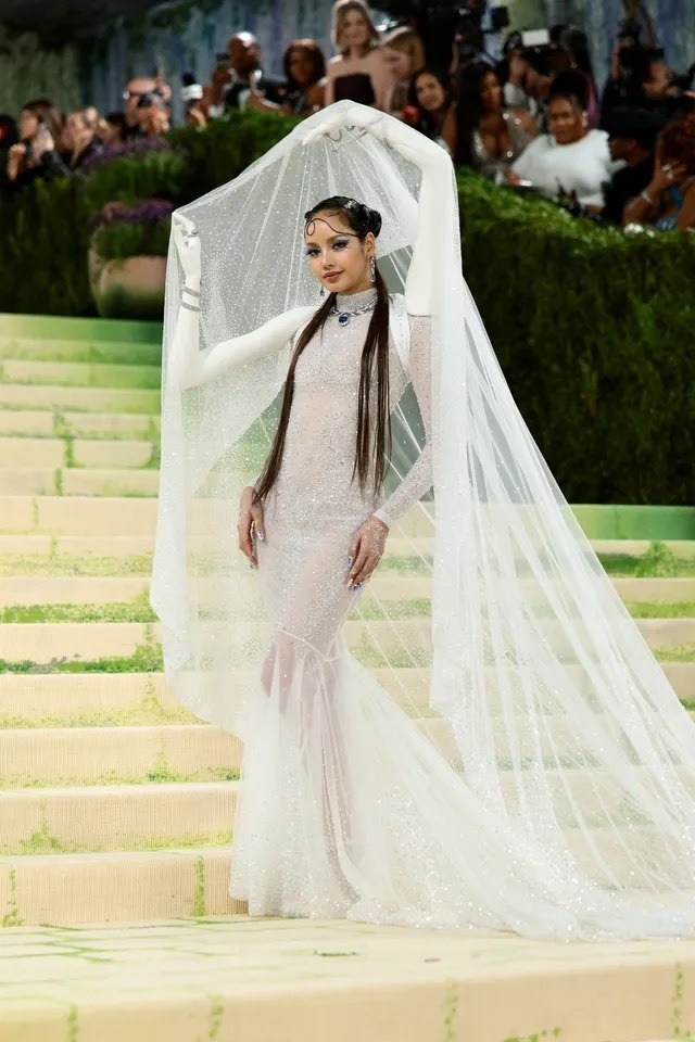 Trong khoảnh khắc bước lên thảm đỏ Met Gala 2026, Lisa  diện bộ đầm haute couture do Robert Wun thiết kế riêng ôm sát cơ thể như một lớp sương mỏng, lấp lánh ánh kim nhẹ nhàng, tôn vinh đường nét hình thể một cách thanh thoát thay vì phô trương. Điểm nhấn độc đáo nằm ở chi tiết cánh tay 3D được quét trực tiếp từ chính cơ thể Lisa và tạo hình theo cảm hứng từ động tác múa truyền thống Thái Lan khiến tổng thể trang phục trở thành một tác phẩm nghệ thuật sống động. 