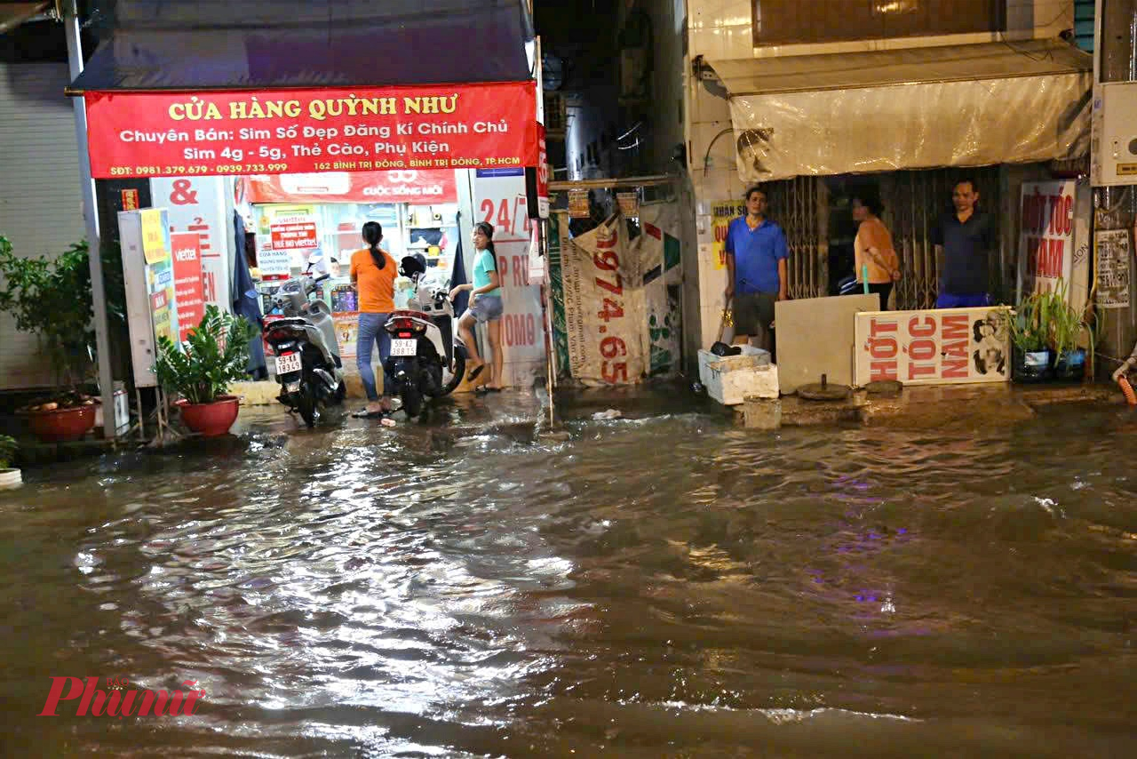 Nhiều hộ kinh doanh ven đường phải khẩn trương kê cao hàng hóa, dùng bao cát chắn nước tràn vào nhà.