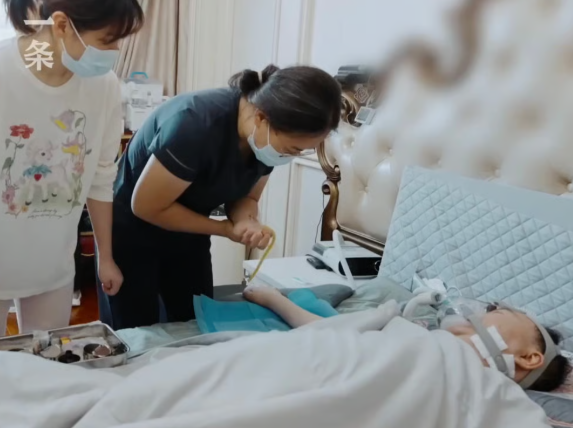 Cai nằm trên giường, được chăm sóc bởi một y tá và một thành viên trong gia đình. Ảnh: Yitiao